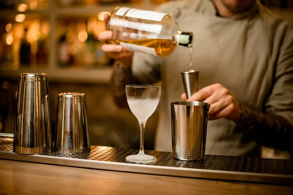 different glasses stands on bar and in background bartender is pouring drink into jigger