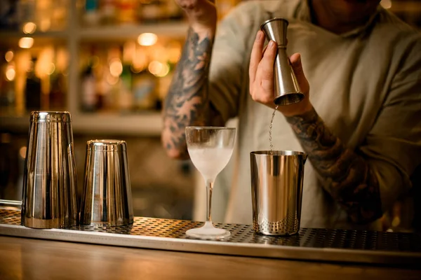 Man bartender hälla dryck från metall jigger i blandningskopp på bardisk — Stockfoto