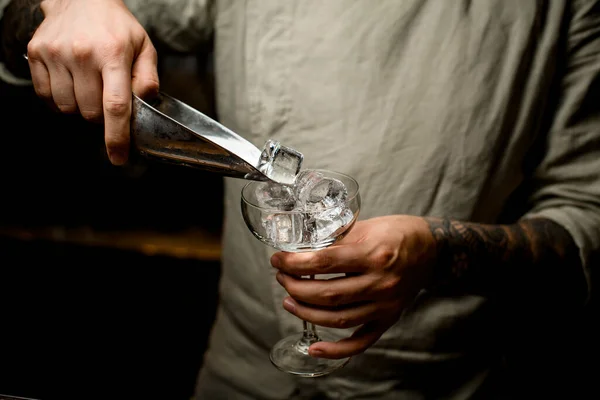 Camarero hombre sostiene cucharada de metal con cubitos de hielo y los vierte en copa de vino — Foto de Stock