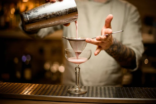 Бармен тримає сито над келихом вина і обережно п'є коктейль від шейкера . — стокове фото