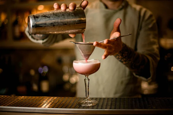 Barman houdt zeef over wijnglas en schenkt zorgvuldig cocktail uit shaker. — Stockfoto