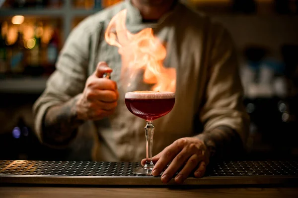 Barista con attenzione fare fuoco su vetro con cocktail di schiuma sul bancone del bar — Foto Stock