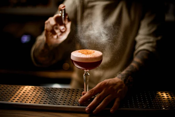 Barman saupoudrer soigneusement sur verre à cocktail avec de la mousse garnie d'orange et de cannelle — Photo