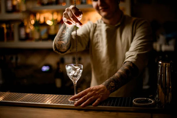 Vista sobre o homem bartender com longa colher bar agitar os cubos de gelo em copo de vinho — Fotografia de Stock