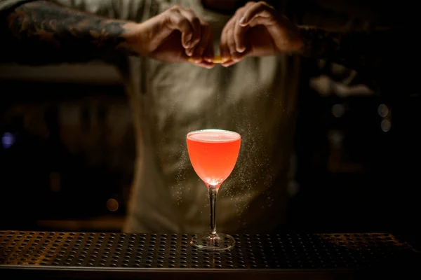 Barman masculino segurando casca de limão sobre vidro com coquetel brilhante e polvilha sobre ele. — Fotografia de Stock