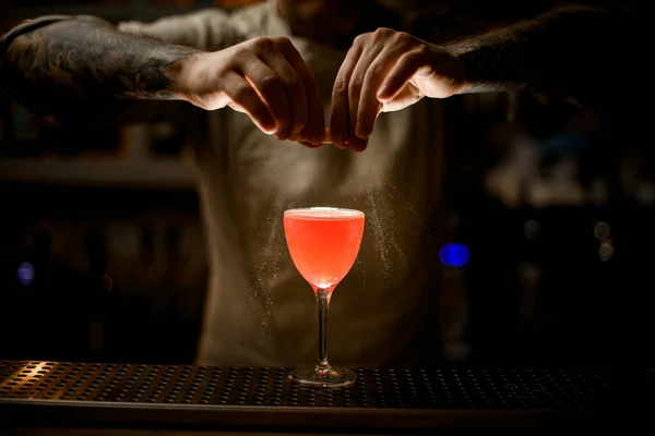 Vista del camarero sosteniendo cáscara de limón y hábilmente espolvorea sobre vidrio con cóctel brillante. — Foto de Stock