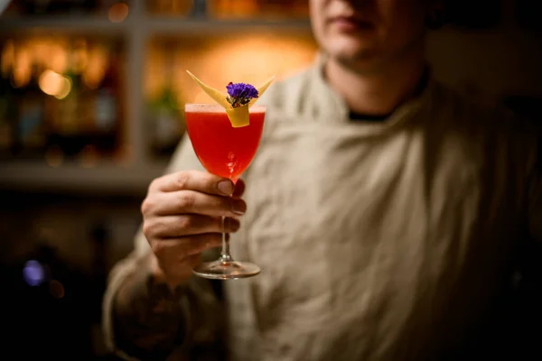 Άνθρωπος κρατά στο χέρι ποτήρι κρασί με ποτό, διακοσμημένο με ξύσμα λεμονιού και λουλούδι. — Φωτογραφία Αρχείου