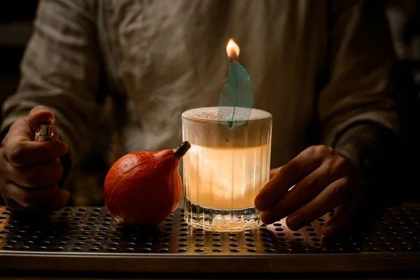 Barmann bestreut sorgfältig altmodisches Cocktailglas mit Schaum und brennendem Blatt. — Stockfoto