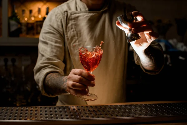 Homem detém copo de coquetel com bebida alcoólica salpicante e adiciona líquido de jigger — Fotografia de Stock