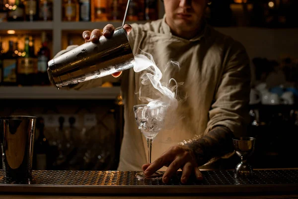 Männlicher Barkeeper gießt dampfenden Drink aus Stahlbecher in Weinglas mit Eiswürfeln. — Stockfoto