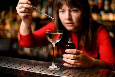 Kırmızı elbiseli bayan barmen içeceğe bir damla malzeme ekliyor.