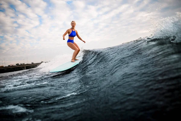 Femme blonde en maillot de bain bleu descend la vague sur planche de surf. — Photo