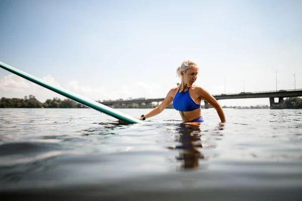 Вид женщины, сидящей на доске для серфинга в речной воде и отводящей взгляд — стоковое фото