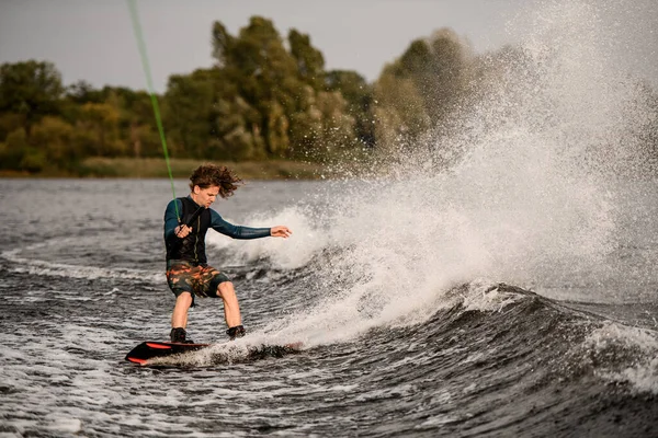Ung atletisk man håller spänd rep och rider ner på våg på wakeboard — Stockfoto