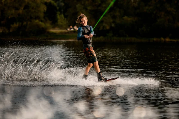 Attivo giovane uomo in muta e gilet cavalca wakeboard sul fiume — Foto Stock