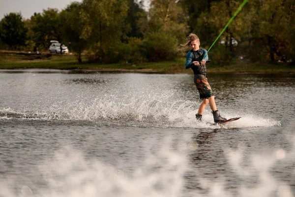 Vista sul giovane in muta e gilet equitazione wakeboard sul fiume — Foto Stock