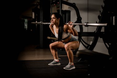 Halterli güçlü kaslı kadın vücut geliştirici spor salonunda çömelme hareketleri yapıyor..