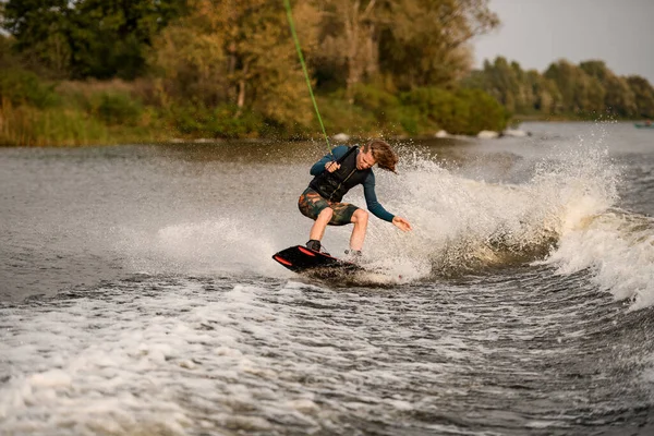 Beau jeune homme se tient avec les genoux pliés sur wakeboard et descendre sur la vague — Photo