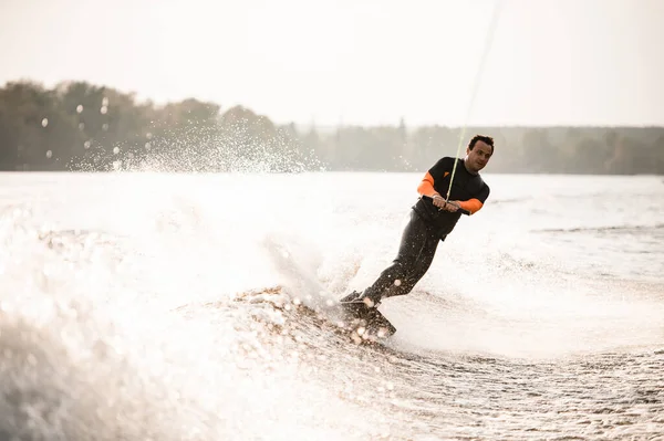 Volwassen man rijdt naar beneden op wakeboard op spetterende rivier golf van de boot — Stockfoto