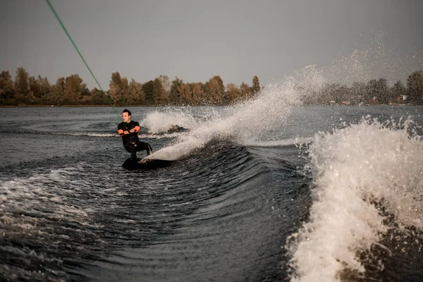 Uitzicht op actieve man rijden naar beneden op wakeboard op spetterende rivier golf van boot — Stockfoto