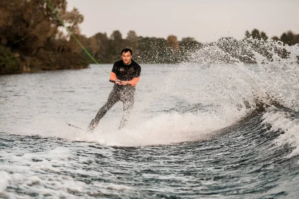 Zicht van de mens in wetsuit houdt kabel in zijn handen en wakeboarden op spetterende golf — Stockfoto