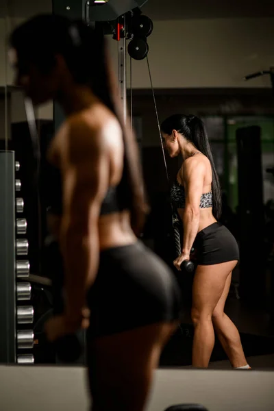 Atletická žena zvedání závaží naproti zrcadlu ve fitness centru. — Stock fotografie