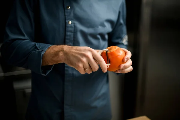 Man holds fruit in his hands and gently peels it with knife — Stock Photo, Image