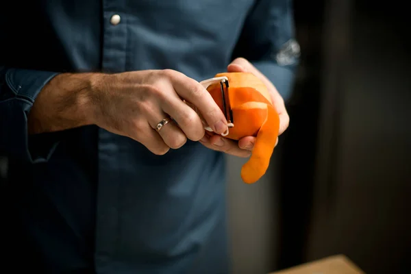 Close-up on male hands holding fruit and cuts off the peel with knife — Stock Photo, Image