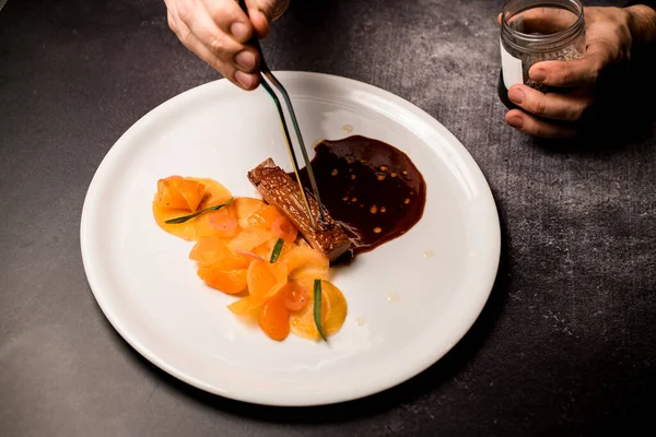 Talerz z naczyniem jest na stole i ręce człowieka ostrożnie umieścić kawałek mięsa w nim — Zdjęcie stockowe