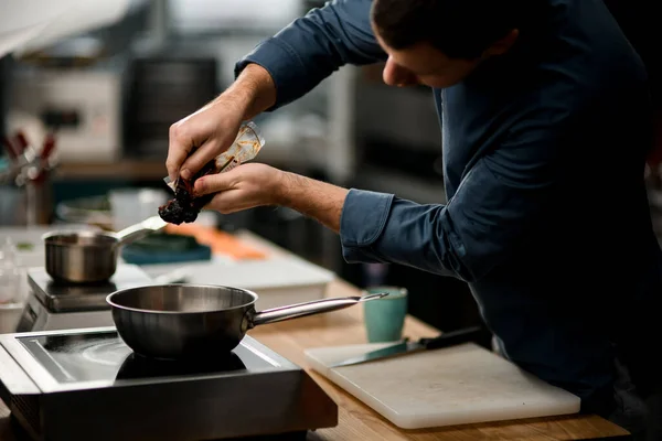 Мужчина-повар держит пакет с продуктом и кладет его на сковородку — стоковое фото
