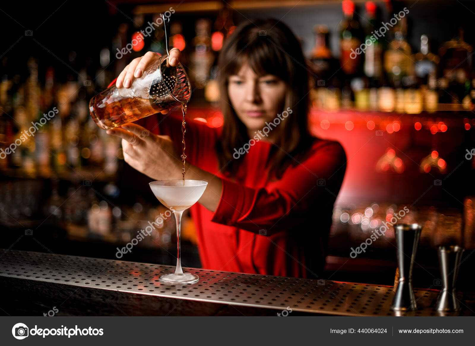 Wineglass stands on bar and woman bartender holds mixing cup and