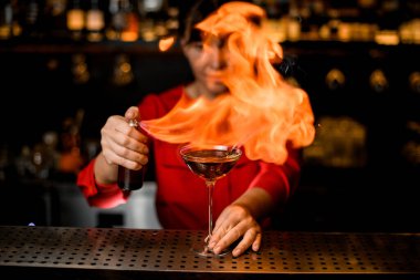 İçkili şarap kadehi barın üzerinde durur ve bayan barmen ustaca serpiştirir ve üzerine ateş yakar.