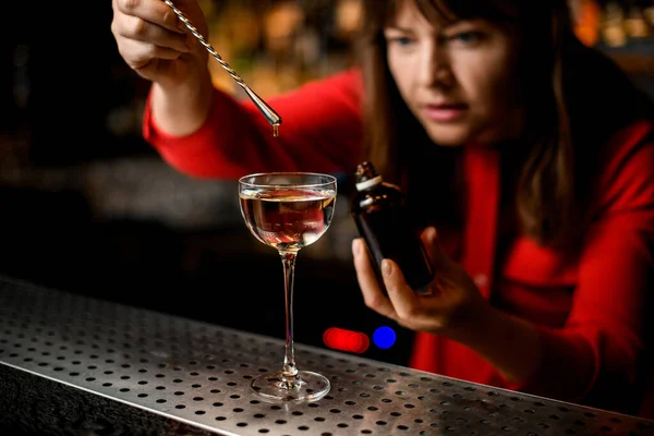 Vidro com estandes líquidos na barra e bartender adiciona ingrediente a ele — Fotografia de Stock