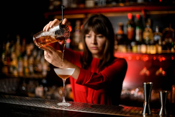 Wineglass stands on bar and bartender holds mixing cup and accurate pours drink into it — Stock Photo, Image