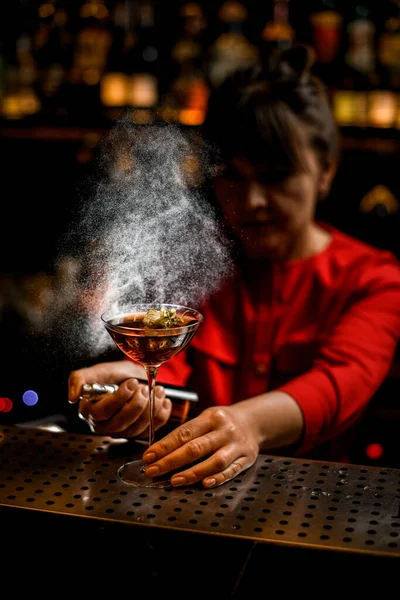 Wine glass with brown drink stands on bar counter and female bartender sprinkles over it — Stock Photo, Image