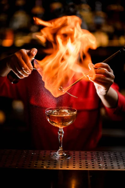 Úžasný pohled na sklo s pitím, přes které barman drží rostliny a postřikuje a zapaluje — Stock fotografie