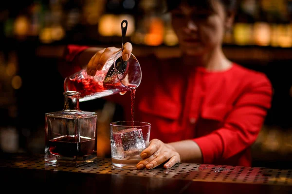 Glass with large piece of ice stands on bar and bartender pours drink into it — Stock Photo, Image