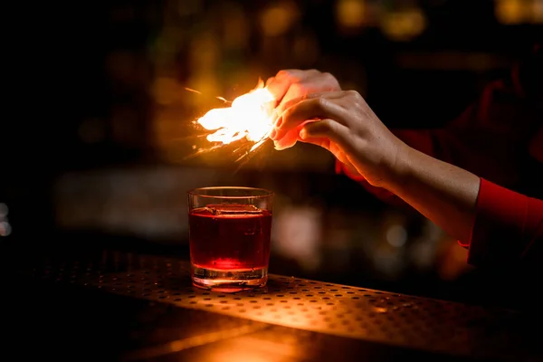 Вид на стекло с напитком, стоящим на барной стойке, и человеческие руки прыгают и поджигают — стоковое фото