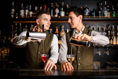 two bartenders pour cocktails into glasses and look at each other clipart