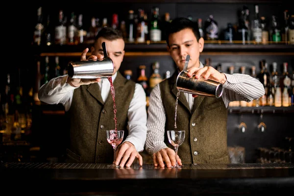 Dois barmen bartenders despeje coquetéis em copos ao mesmo tempo no bar — Fotografia de Stock