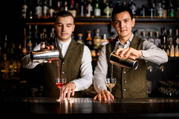 Vista de bartenders derramando coquetéis em copos ao mesmo tempo no bar — Fotografia de Stock