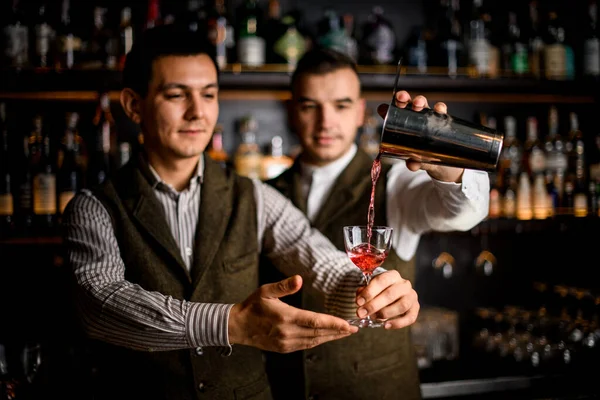 man bartender holds glass and another man bartender pours cocktail into it