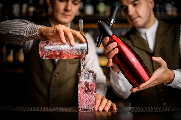 Close-up em vidro em que dois bartenders simultaneamente derramar líquido de sifão e xícara — Fotografia de Stock