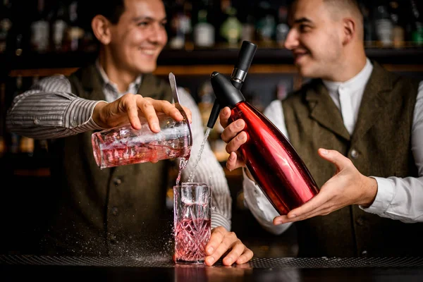 Bela vista de vidro em que dois bartenders simultaneamente derramar líquido de sifão e xícara — Fotografia de Stock