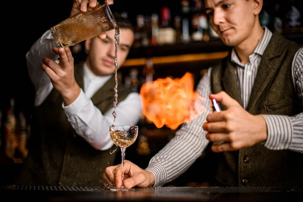 Barman nalévá nápoj do skla a jiný muž ho zapaluje — Stock fotografie