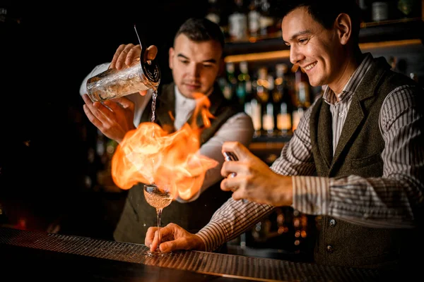 Vista impressionante di uomo barista sorridente che dà fuoco bicchiere da cocktail al bar — Foto Stock