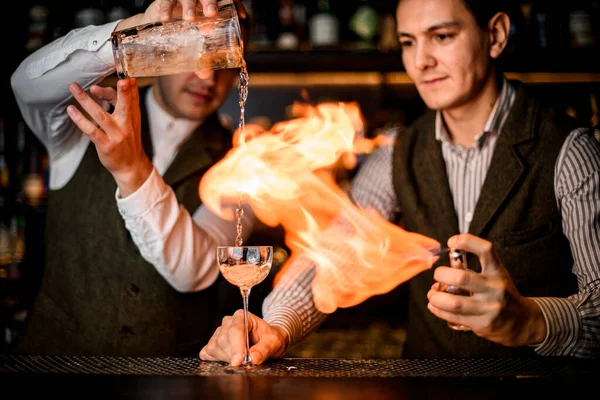El vidrio está en la barra y dos camareros vierten la bebida y la prenden fuego — Foto de Stock