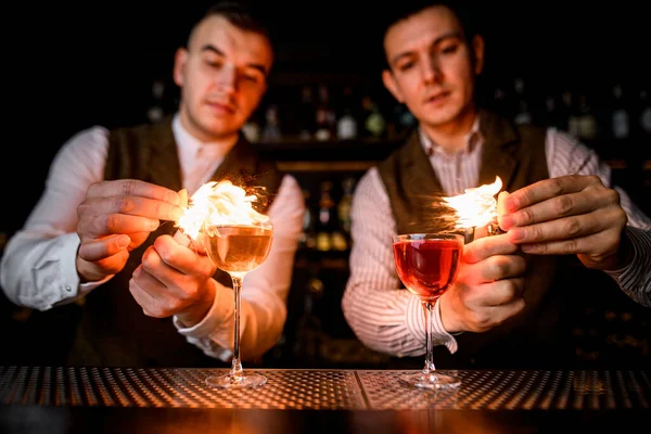 Copos com estandes de bebidas no bar e bartenders profissionais polvilhar e colocá-los em chamas — Fotografia de Stock