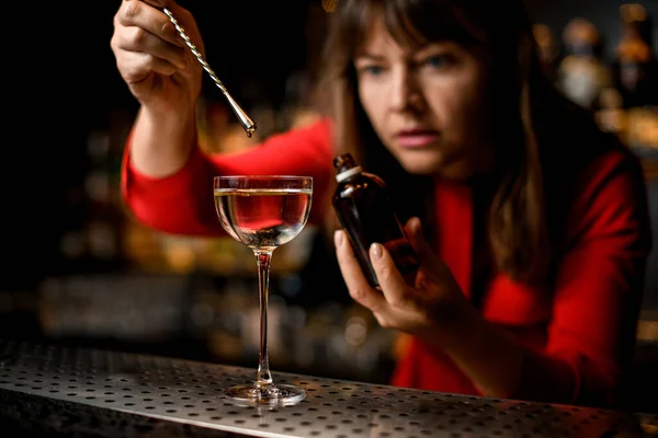 Vidro com estandes líquidos na barra e bartender fêmea adiciona ingrediente a ele — Fotografia de Stock