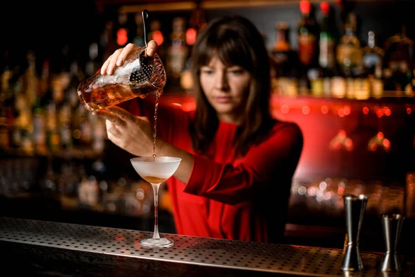 Wine glass stands on bar and female bartender holds mixing cup and pours drink into it — Stock Photo, Image